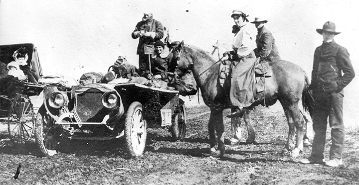 old black & white photo someone in a car and someone on a horse
