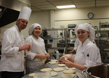 two students and an instructor preparing something in the kitchen