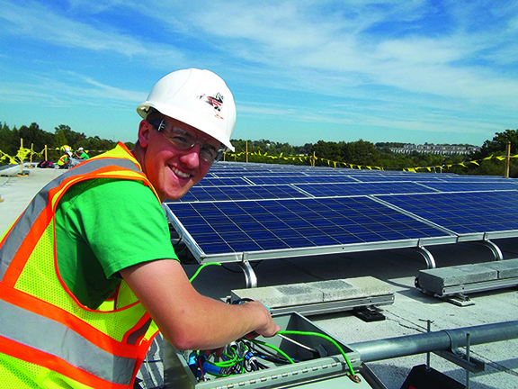 student wearing a hard helmet next to a solar panel