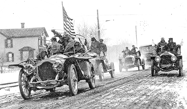 people driving old cars on a dirt road, american flag