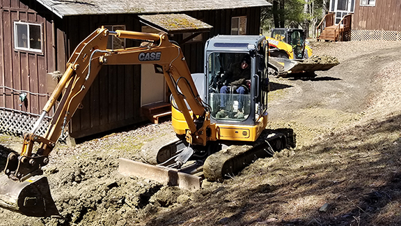 student operating a bulldozer in front of a cabin