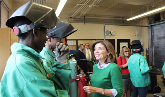 Lt. Gov. Kathy Hochul tours Burgard High School; students in green uniforms and welding helmets and Lt. Gov. Kathy Hochul