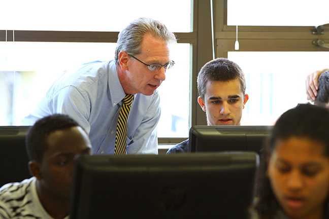 Associate Professor of Business Steven Reynolds provides assistance to a student on a computer in a lab.