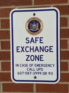 Safe Exchange Zone sign on brick wall, in case of emergencye call UPD 607-587-3999 or 911.